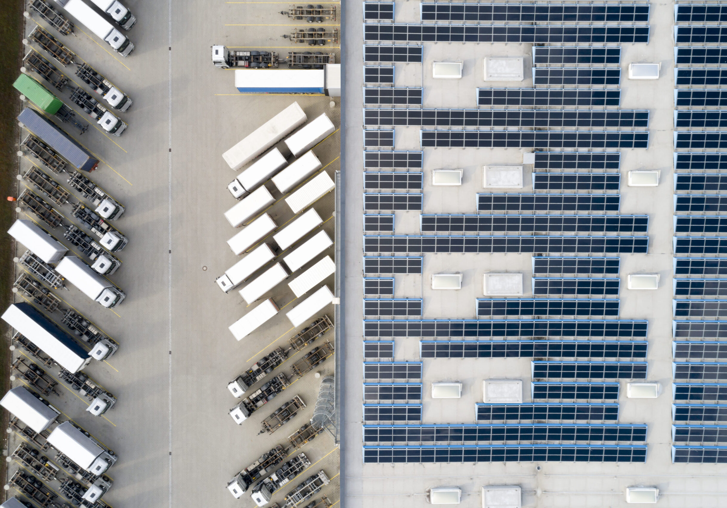 Aerial view of semi trucks during unloading and a large storehouse with solar panels on the rooftop.